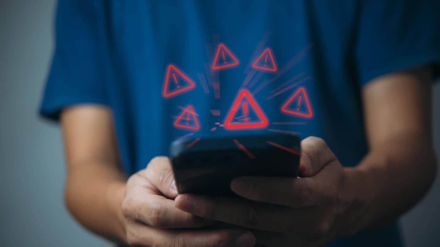 Person using smartphone with triangle caution warning sign for notification error and maintenance concept.
